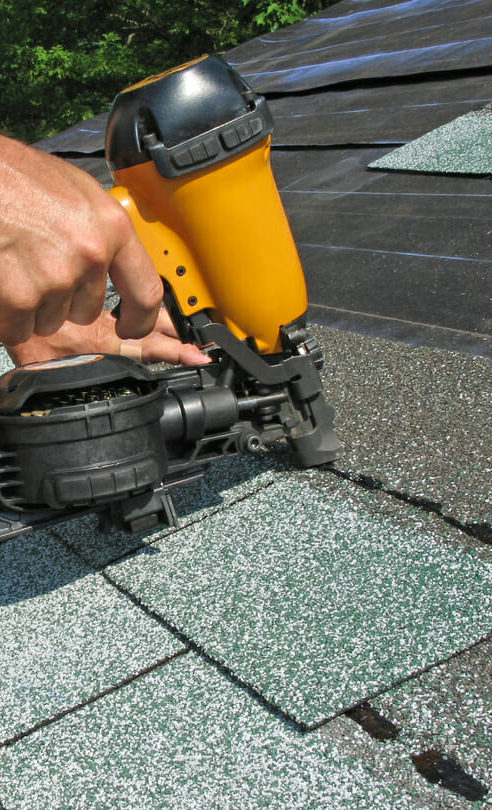 A hand holding a yellow power tool, stapling a roof shingle on